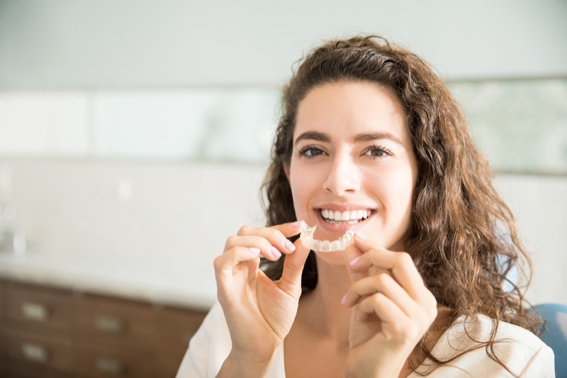 Smiling woman holding a clear aligner